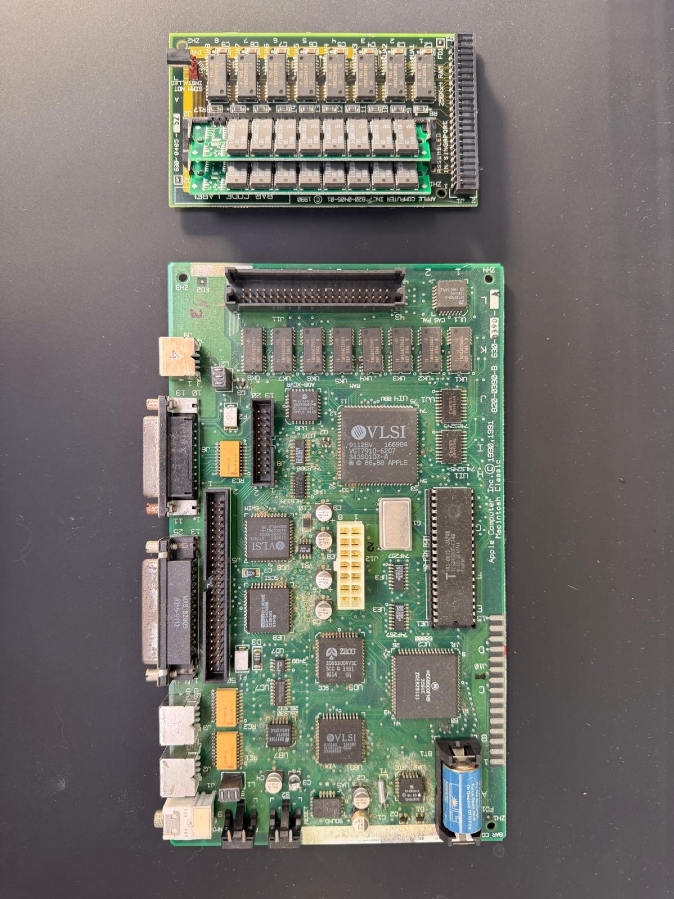The Macintosh Classic logic board before restoration, with the old blue PRAM battery still fitted